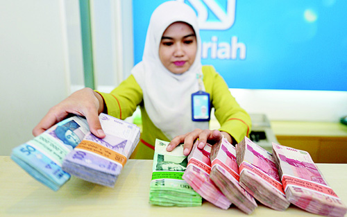 File photo shows an employee of BRI Syariah bank managing bundle of Indonesian Rupiah bank notes in Jakarta. Indonesian regulators have launched a plan aimed at growing the Islamic finance sector, which currently accounts for less than five percent of banking assets, compared to a quarter in neighbouring, more developed Muslim-majority Malaysia and around half in Saudi Arabia. (AFP)