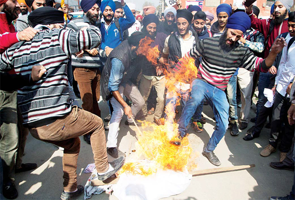 Kashmiri Sikhs kick a burning effigy of Gurmeet Ram Rahim Singh, chief of the religious sect Dera Sacha Sauda, during a protest against the killing of two Sikh boys,