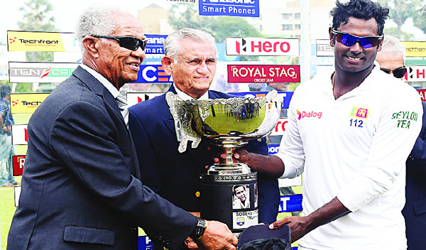 Sri Lankan cricket captain Angelo Mathews (right), West Indian cricket legend Garfield Sobers (left), and former Sri Lanka cricket captain Michael Tissera (center), hold up the Sobers/Tissera Trophy after Sri Lanka’s victory in the Test match series between Sri Lanka and the West Indies at The P. Sara Oval Cricket Stadium in Colombo on Oct 26. Sri Lanka defeated the West Indies by 72 runs in the second and final Test in Colombo to sweep the series 2-0. (AFP)