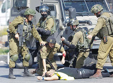 A wounded Israeli soldier kneels over the body of a Palestinian who stabbed him during clashes in Hebron, West Bank on Oct 16.