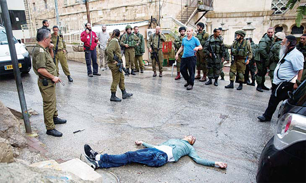 Israeli soldiers and settlers gather around the body of a Palestinian man who tried to stab a soldier at the Jewish settlement of Beit Hadassah