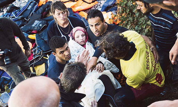 Paramedics and volunteers carry a Syrian woman who has recently given birth on a beach after she arrived on the Greek island of Lesbos, after crossing the Aegeans sea from Turkey on Oct 13. (AFP)